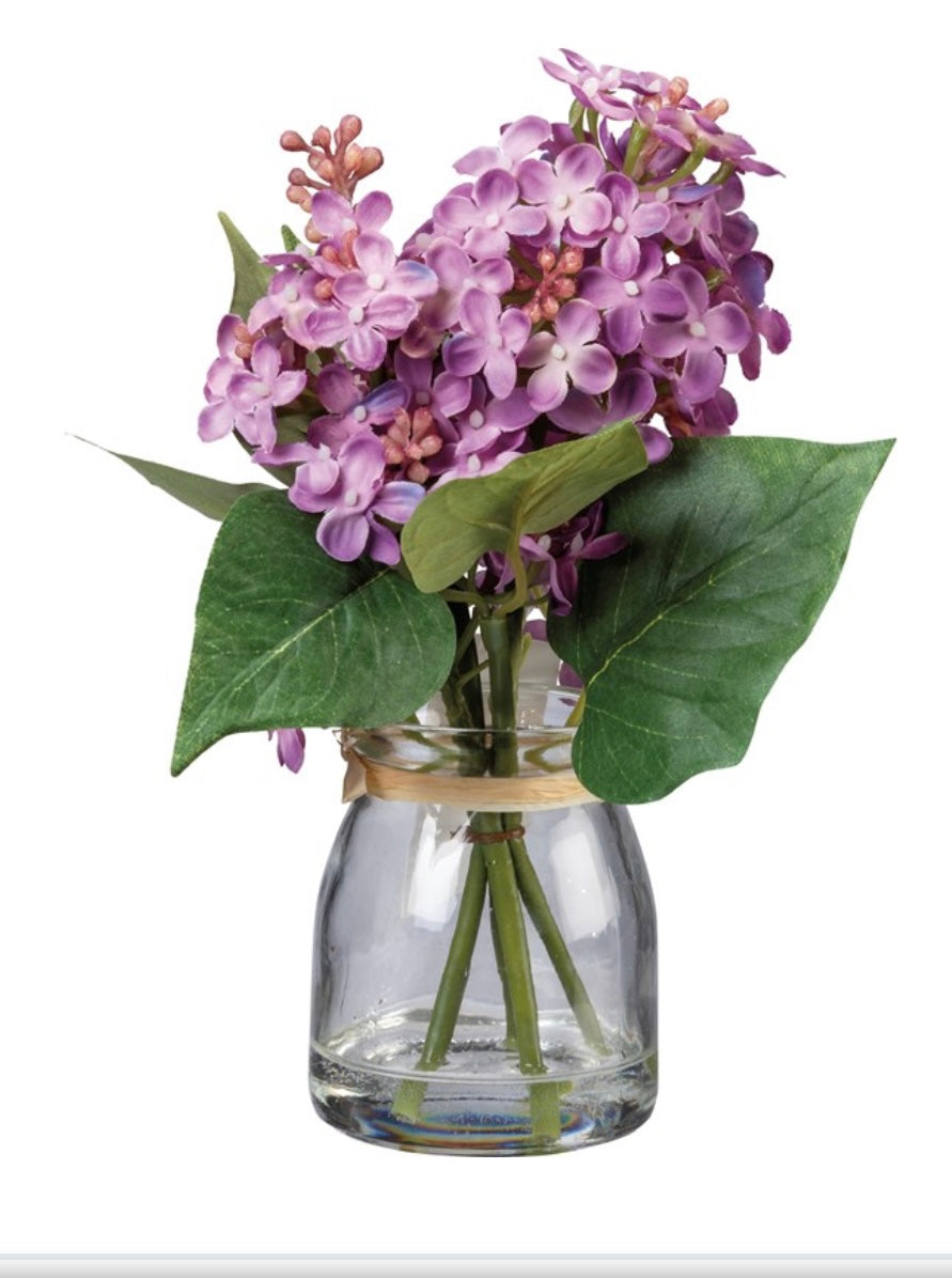 Purple lilacs and green leaves in a clear glass jar with water. Available sizes: small, medium, large.
