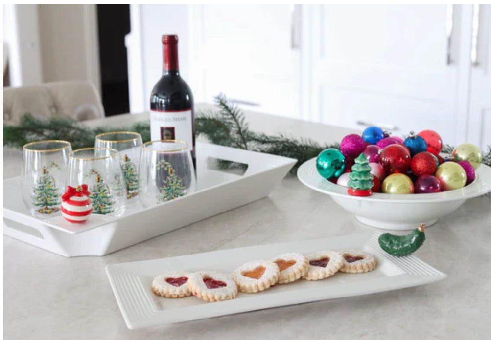 Elegant Bread Tray Stripes holding a red wine bottle and decorated wine glasses. Also includes a rectangular plate of assorted cookies and a bowl of colorful Christmas ornaments on a greenery-adorned kitchen counter. Available sizes: Standard.