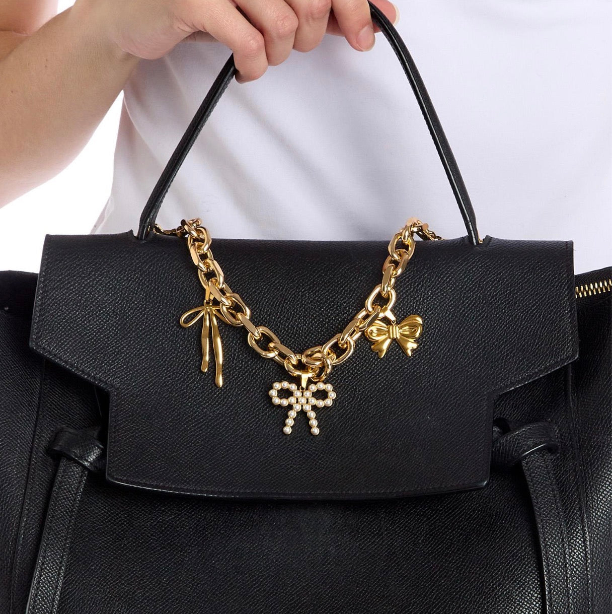 Black textured handbag with Charmed Life Chain Bag Charms: gold chain, bow-shaped charms (one with pearls). Available in small, medium, and large.