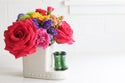 Jumpin Puddles Minis: red roses, purple and yellow flowers in a white sewing machine vase with green spools. Sizes available.