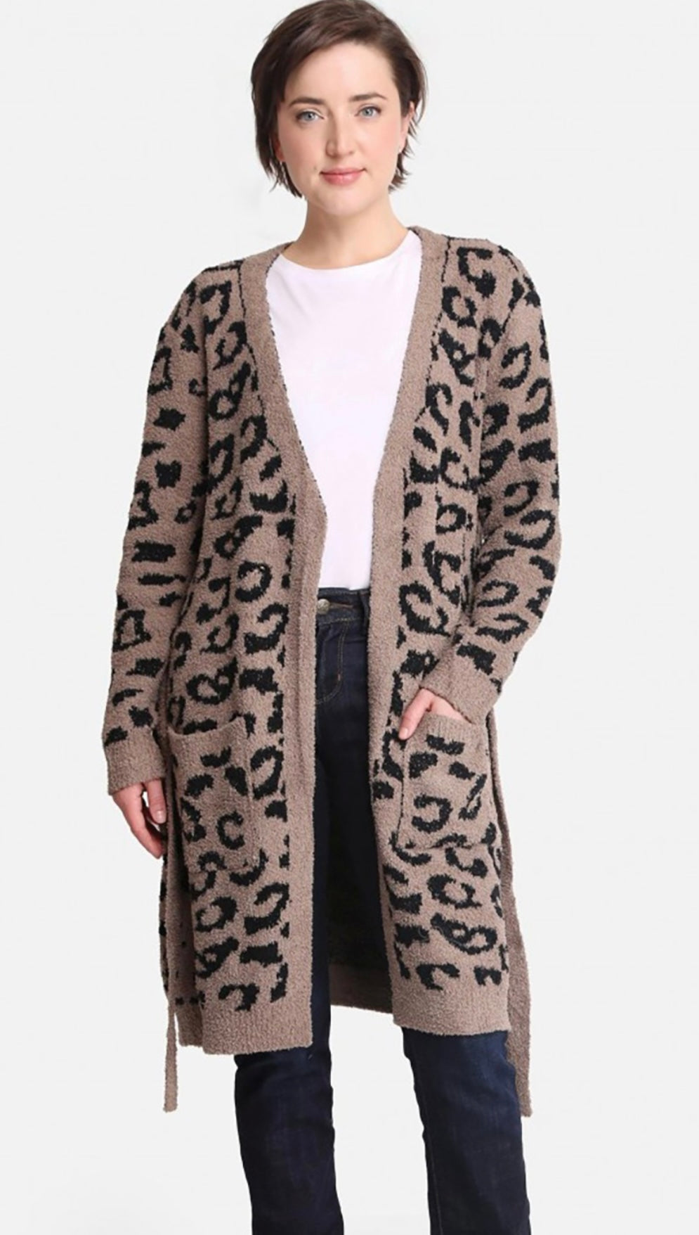 A woman stands confidently in a long leopard print Comfy Luxe Robe over a white t-shirt, paired with dark jeans. She has short hair and a subtle smile.