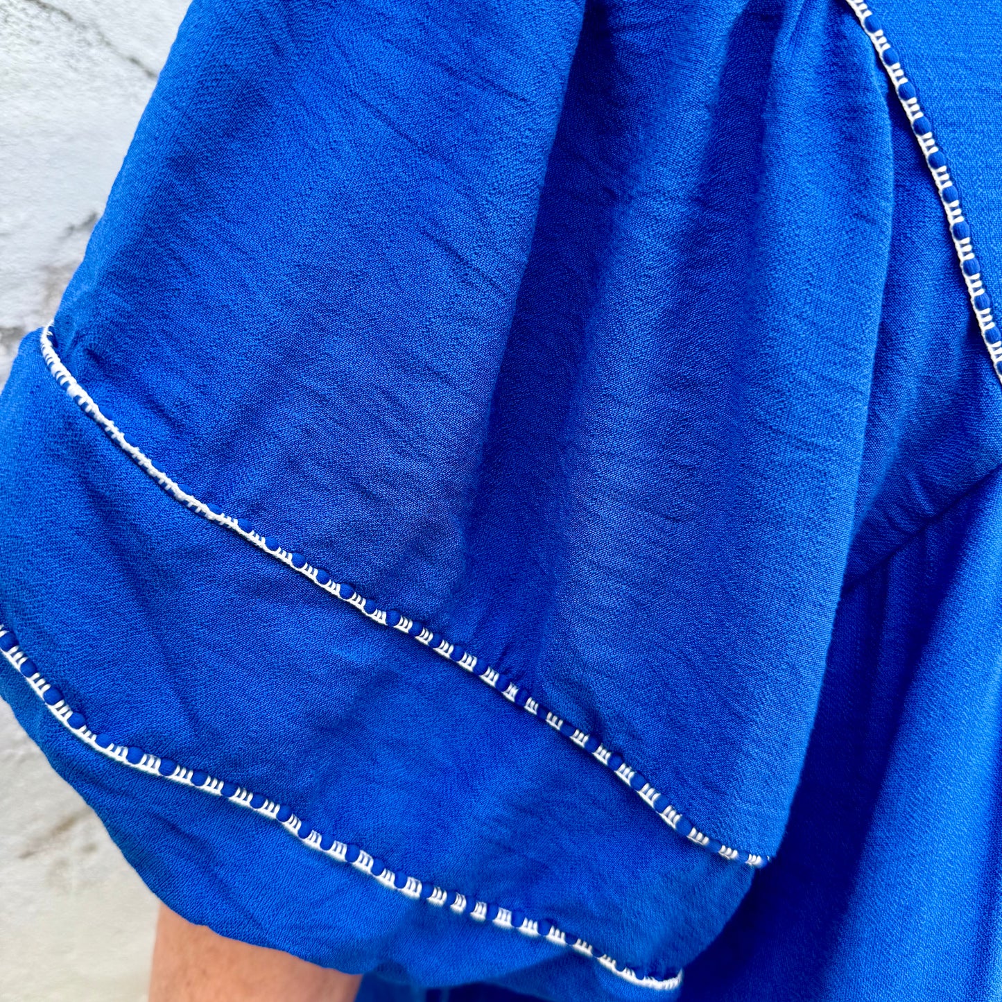 Close-up of Blue Belle Lace Trim Blouse with wide, ruffled sleeves, lace trim, and white stitching. Available in S-XL.