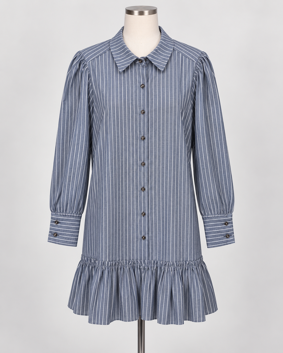 The Drop Waist Shift Dress has blue and white vertical stripes, long sleeves with buttoned cuffs, a classic collar, button-down front, and a ruffled hem. Available in sizes XS-XL.