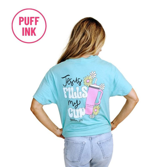 Back view of a woman wearing a Jesus Fills My Cup T-Shirt with the text "Jesus fills my cup" and a graphic of a cup with flowers. A "puff ink" logo is in the top
