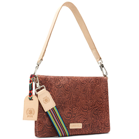 The Metro Crossbody, Sally features brown embossed tooled leather with floral patterns, a beige strap, colorful woven keychain, tan leather tags, and the Consuela brand logo on the front. Can be used as a crossbody or wristlet. Sizes available: small and medium.