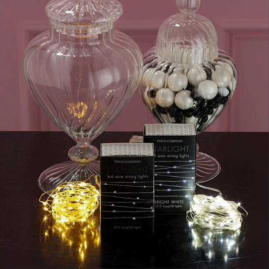 Two glass jars: one filled with black and white gumballs, the other empty. In front, two boxes labeled "Starlight LED Wire String Lights in Gift Box" with sets in yellow and bright white glow. Sizes available: N/A.