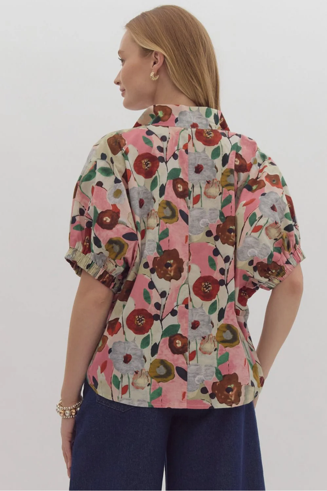 The Flora Top features a vibrant floral pattern in shades of pink, red, and gray with a v-neck and short, ruffled sleeves. Available sizes: XS, S, M, L, XL.