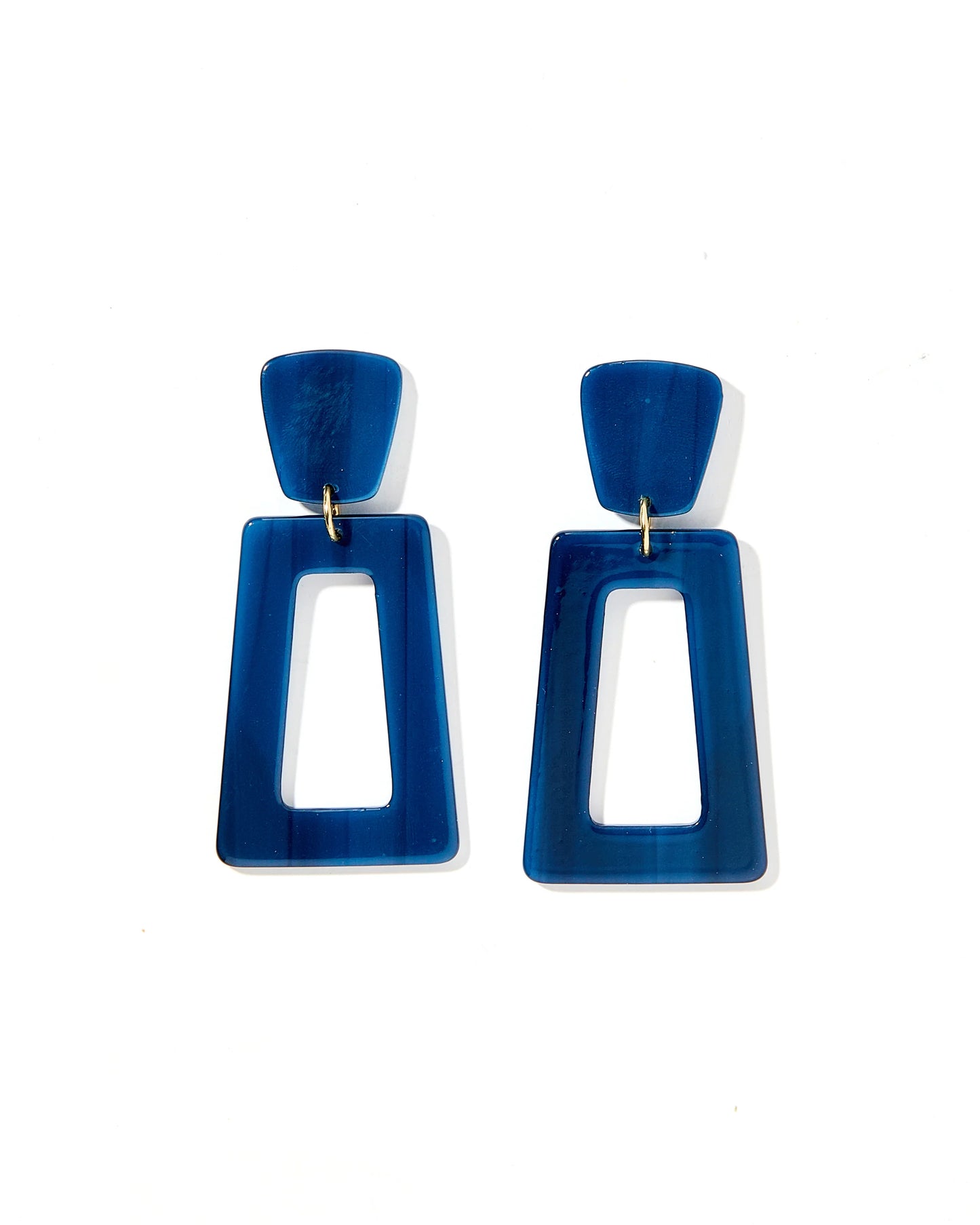 The Kennedy Earrings are geometric blue statement pieces designed for sensitive ears. They feature a small blue trapezoid linked to a larger hollow rectangle in stainless steel, offering minimalist elegance and lasting comfort. Sizes available: One size fits all.