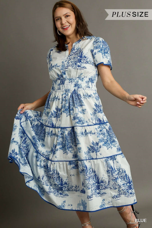 The Landscape Print Tiered Dress features a blue and white pattern, with distinctive balloon sleeves. The dress has a flowy design organized in tiers. Available in plus sizes.