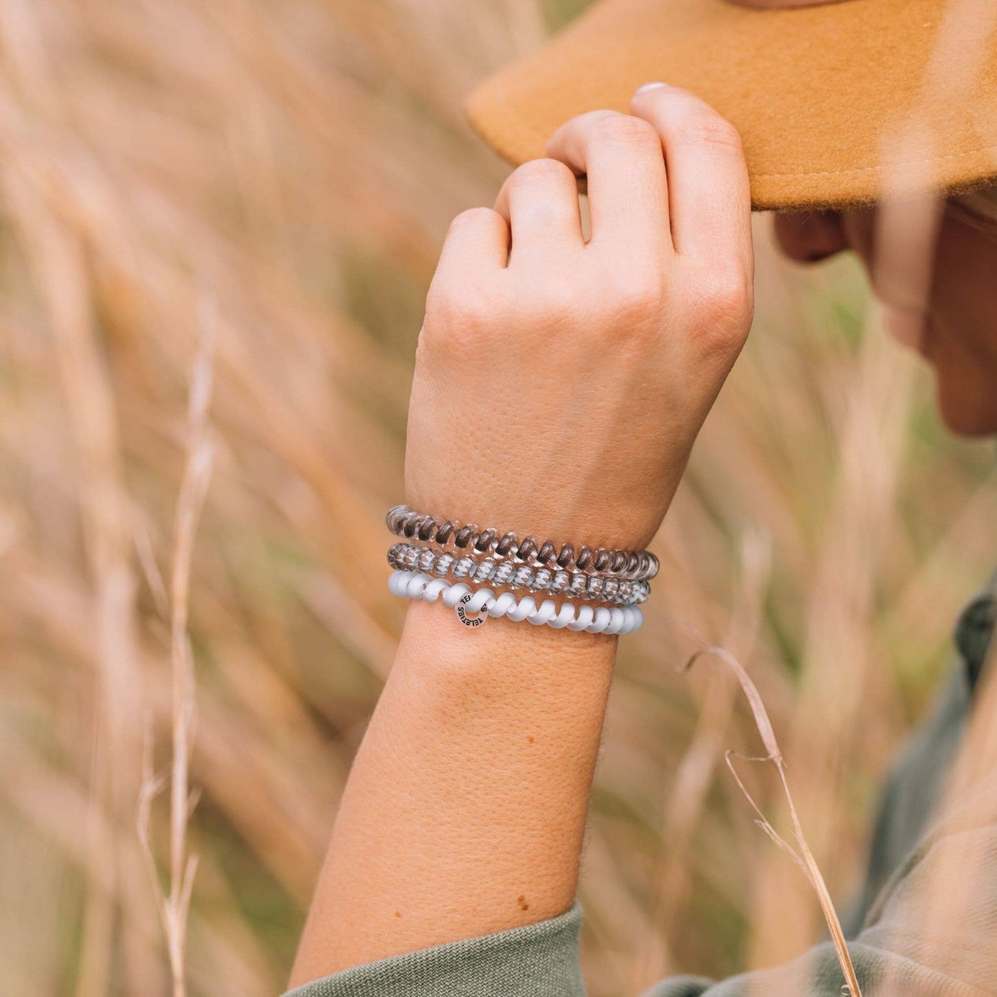 Three coiled TELETIES Hair Ties in gray, brown, and white; available in small and large sizes.