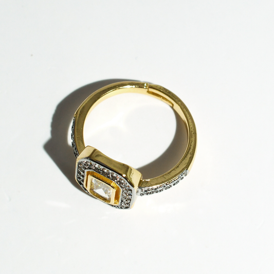Gold-plated ring with square setting, radiant center stone, and smaller surrounding stones. Available in sizes 5-9.