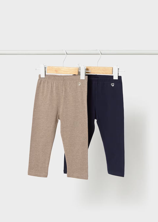 The Little Girl 2-Pack Basic Leggings Set features two pairs of cotton leggings, one light brown and one navy blue, each with a small heart emblem near the waistband. Available in sizes 2T to 6X.