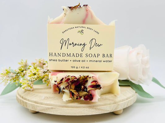 This Saratoga natural body care handmade soap bar is morning. It’s made with shape butter olive oil mineral water is 4.2 ounces it’s moisturizing nursing and gentle. It also is cream with light pink with flower petals.