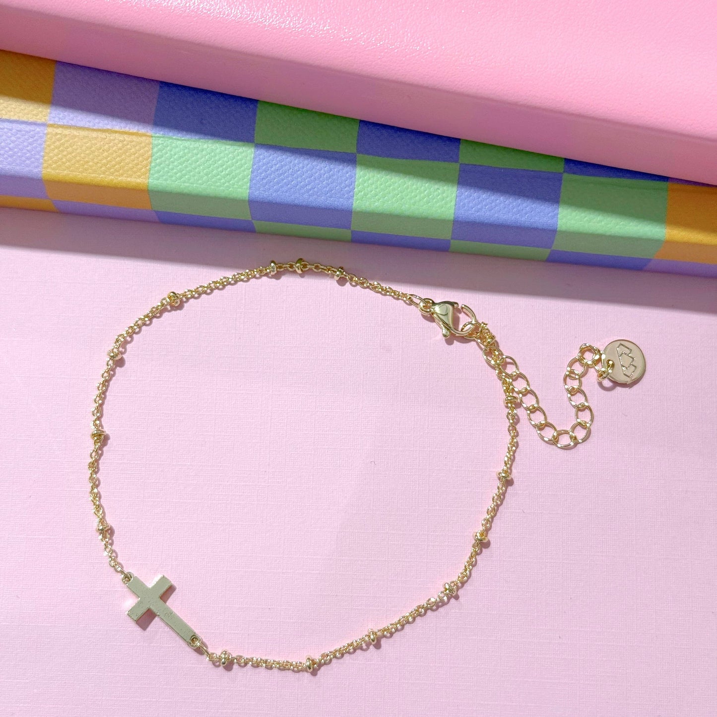 Delicate gold-plated bracelet with sideways cross charm and adjustable clasp. Available in S, M, L sizes.