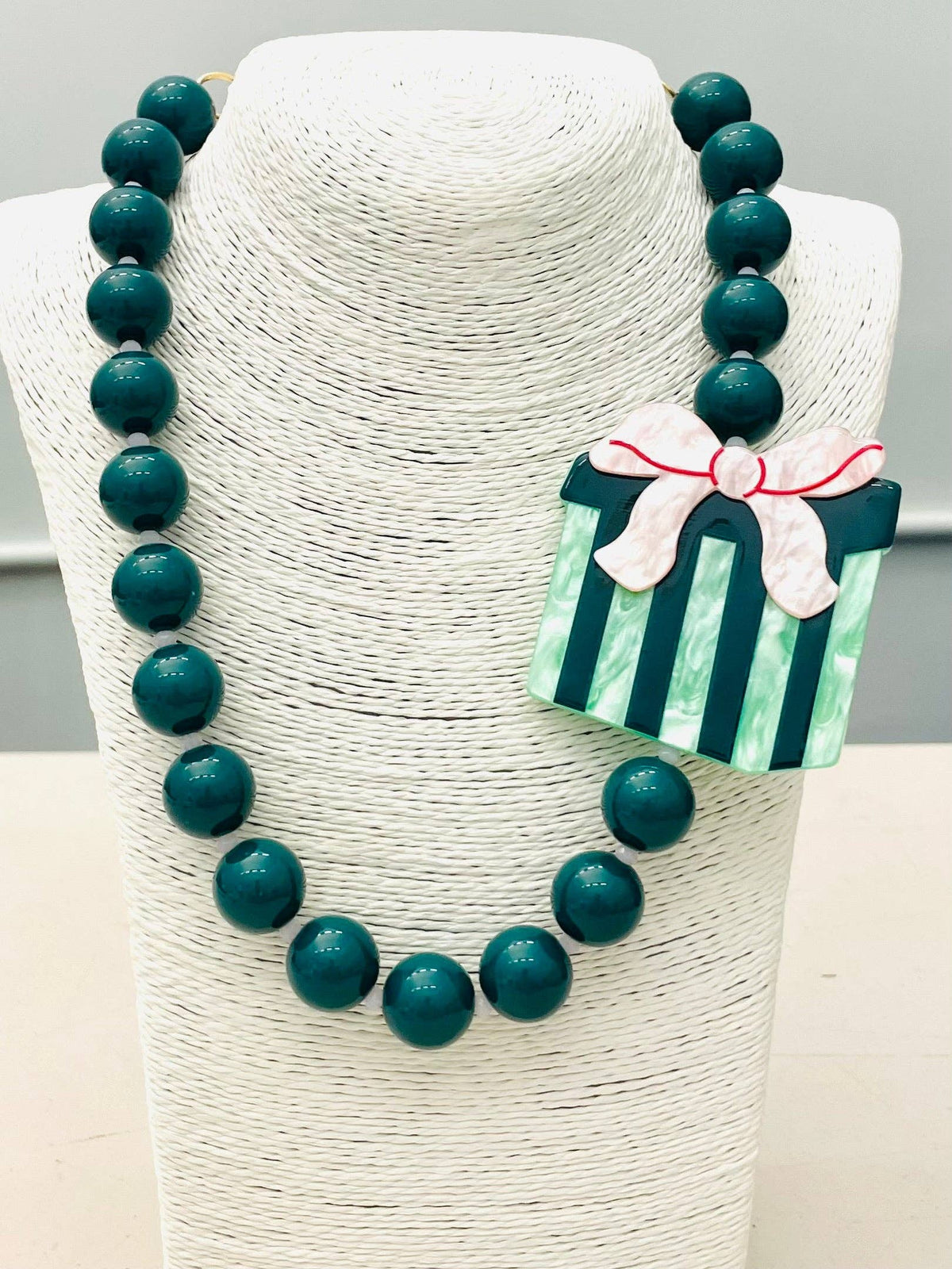 Chunky green beaded necklace with a green and white striped present pendant topped with a pink bow. Sizes available.