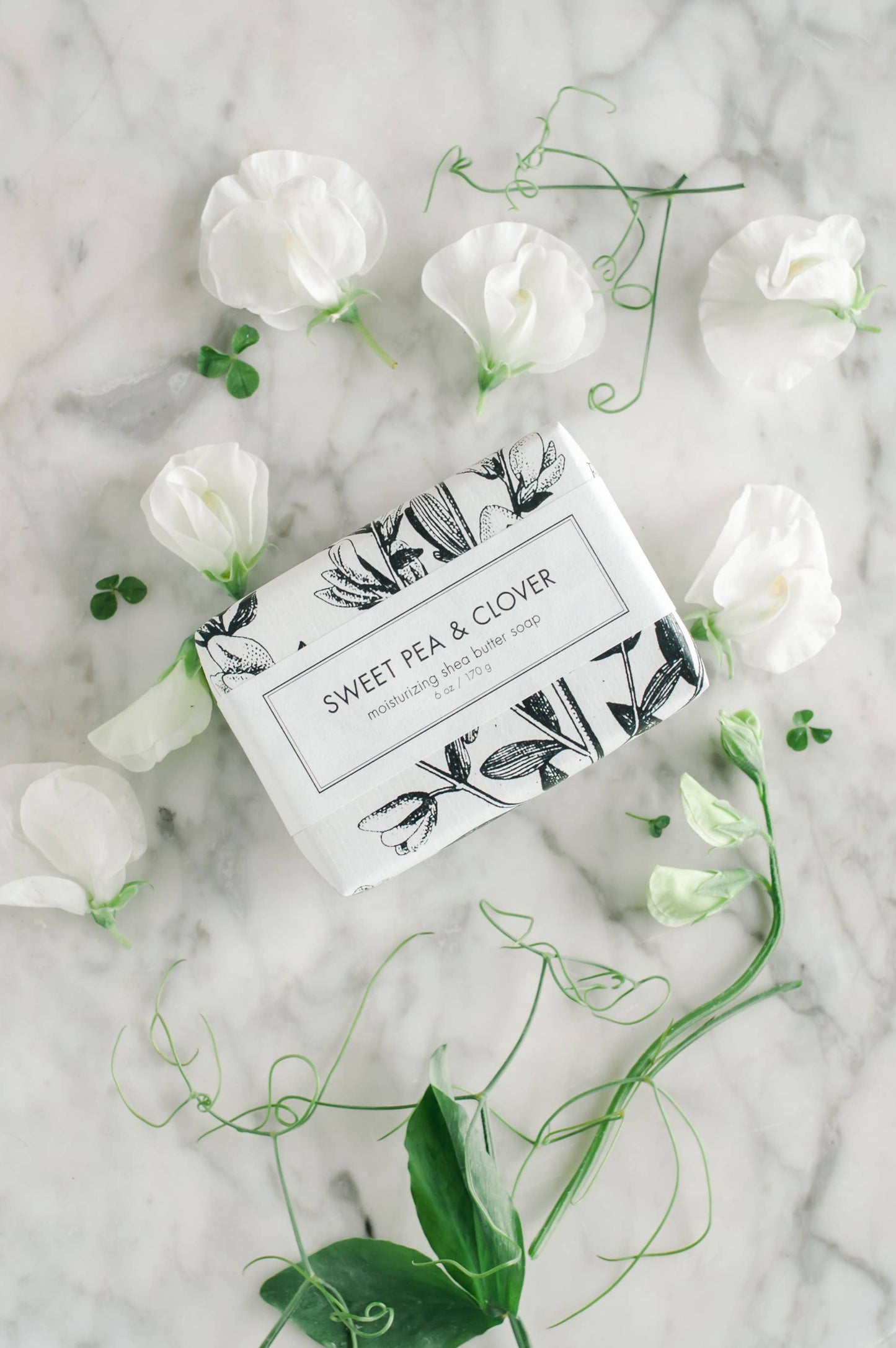 Sweet Pea & Clover Soap - Bath Bar is a fragrant, natural soap enriched with the scent of sweet pea and clover. This bath bar promises a luxurious bathing experience. It comes in one size, perfect for daily use. Enjoy the calming aroma of sweet peas surrounded by notes of greenery, underpinned by subtle whispers of clover. The soap bar rests on a marble surface with an elegant presentation that enhances its appeal.