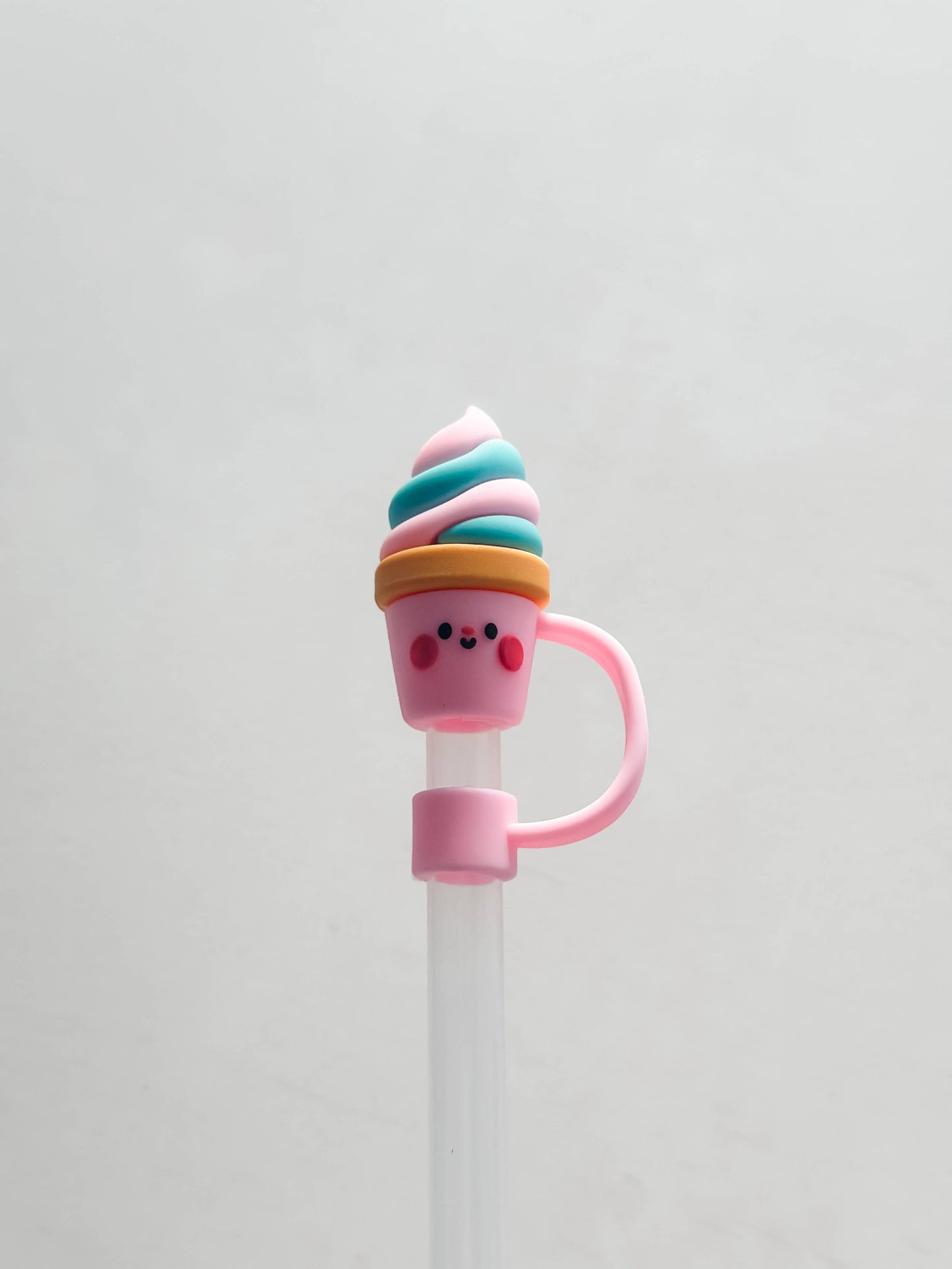 Silicone straw cover shaped like a smiling ice cream cone with pink cheeks and blue, white, and pink swirl. Available in standard size.