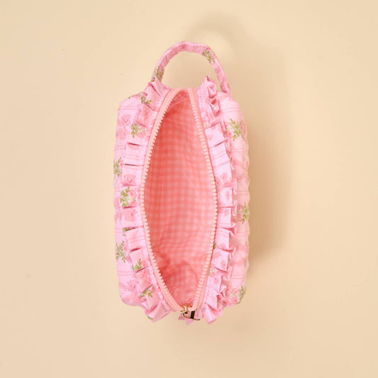 Small pink floral quilted pouch with ruffles, handle, zipper, and wipeable gingham interior. Available in one size.