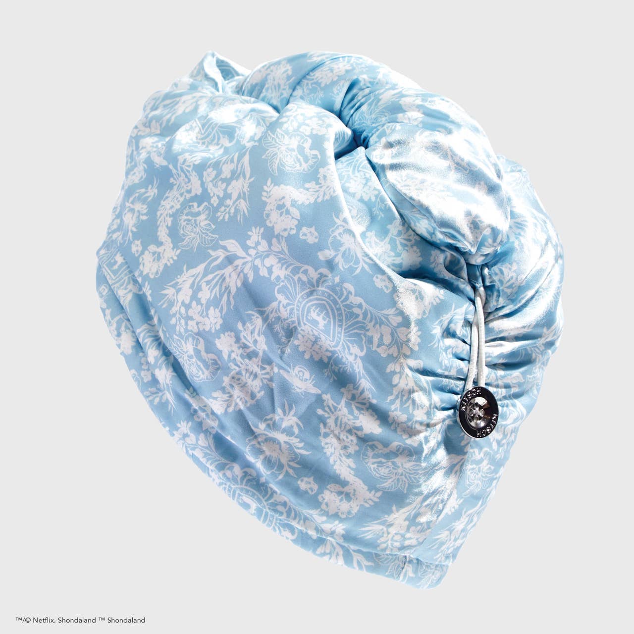 Light blue satin hair towel with white floral pattern, drawstring, and silver button. Available in one size.