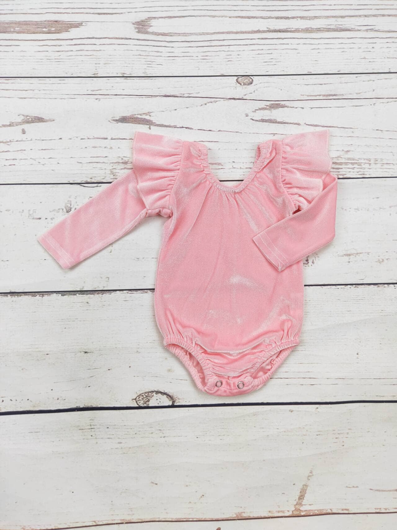 Baby Pink Velvet Onesie with ruffled shoulders, V-neckline, snap closures. Sizes: newborn–24 months.