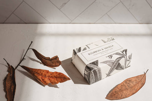 Shea Butter Soap titled "Bourbon & Vanilla Soap - Bath Bar". Comes in a box packaging. Presented with dried leaves for aesthetic purposes.