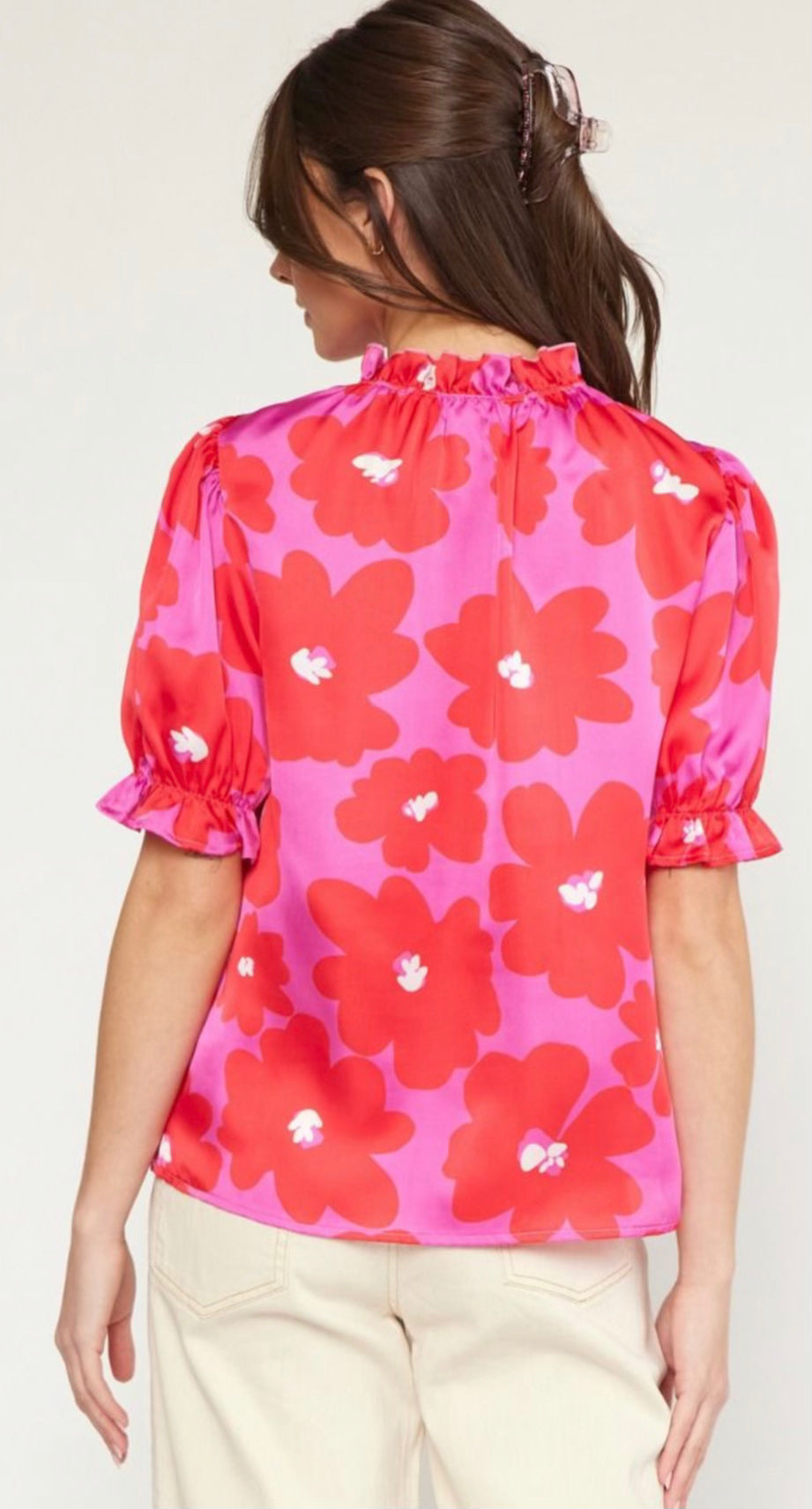 Woman from behind wearing a Poppy Ruffle Blouse with large red and white floral pattern, puffed sleeves, and a gathered neckline, paired with light beige pants, showcasing unique sizing features.