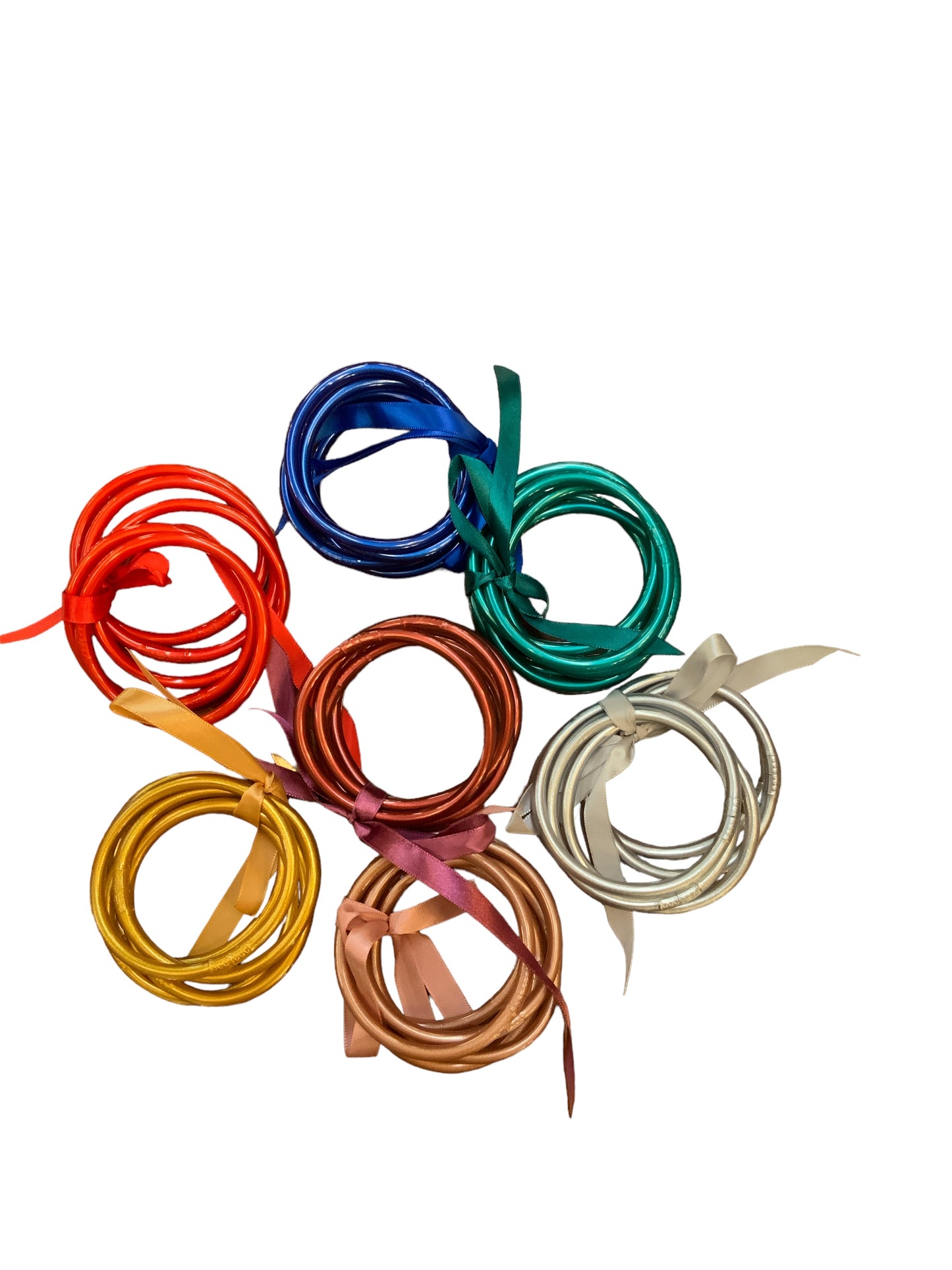This product is a collection of 5 Strand Synthetic Bangles. Each bangle is uniquely designed with various loops and swirls. The set features a vibrant array of colors including red, blue, green, orange, yellow, white, and brown. The bangles sit elegantly against a plain background. Available sizes for this product are small, medium and large.