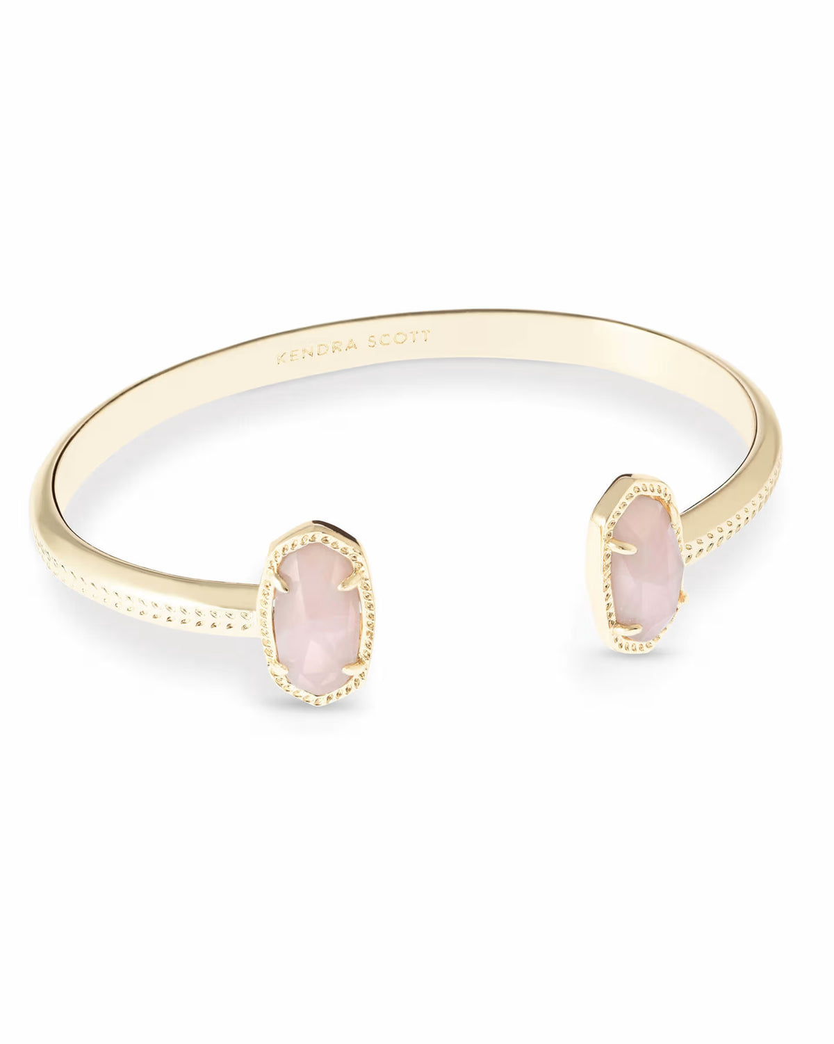 The Elton Gold Cuff Bracelet in Rose Quartz by Kendra Scott is an adjustable gold cuff with two oval light pink Rose Quartz stones, textured edges, and “Kendra Scott” engraved inside. Size options available.