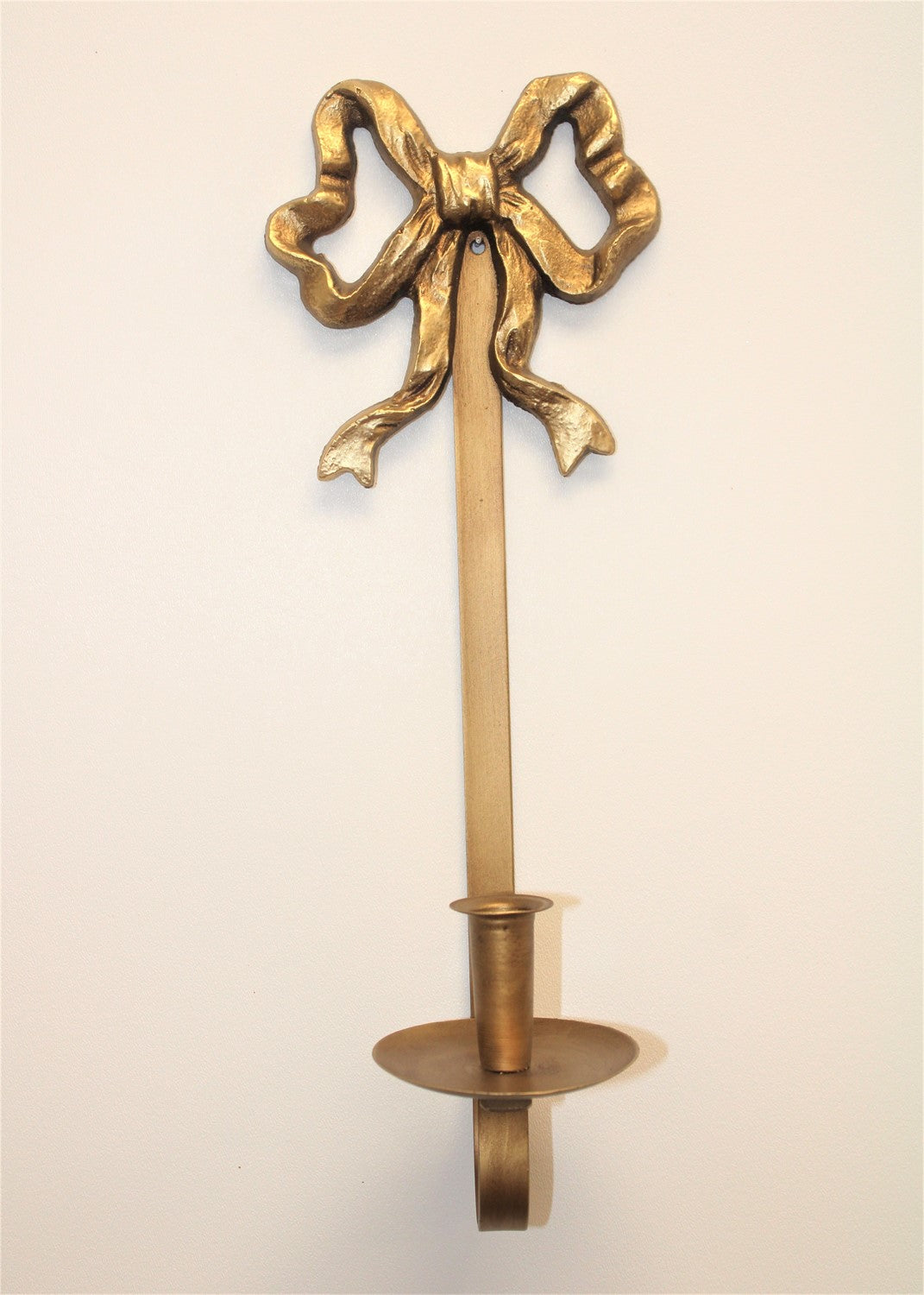 The Iron Bow Wall Taper Holder is a wall-mounted candle holder featuring a ribbon design and round base for taper candles. Sizes available: One size.