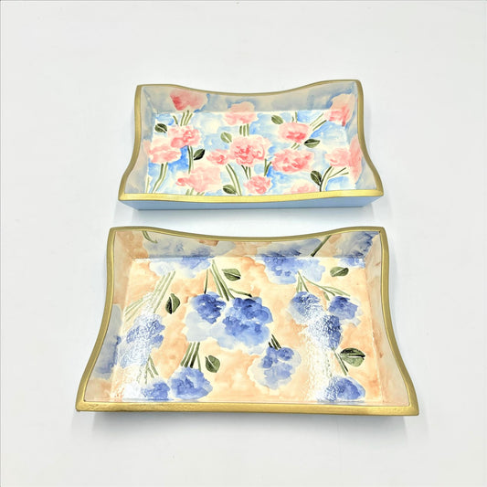Handpainted wood trays with floral designs, featuring pink flowers, green leaves, and blue and lavender blooms on a white backdrop. Curved edges with gold rims. Size: 5.75x8.75x1 inches.