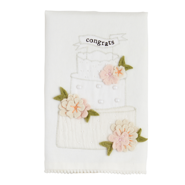 The Wedding Beaded Tea Towel is made of premium cotton and features a three-tiered cake with pink flowers, green leaves, and a "congrats" banner. It includes an embellished appliqué for added elegance. Size: Standard tea towel dimensions.