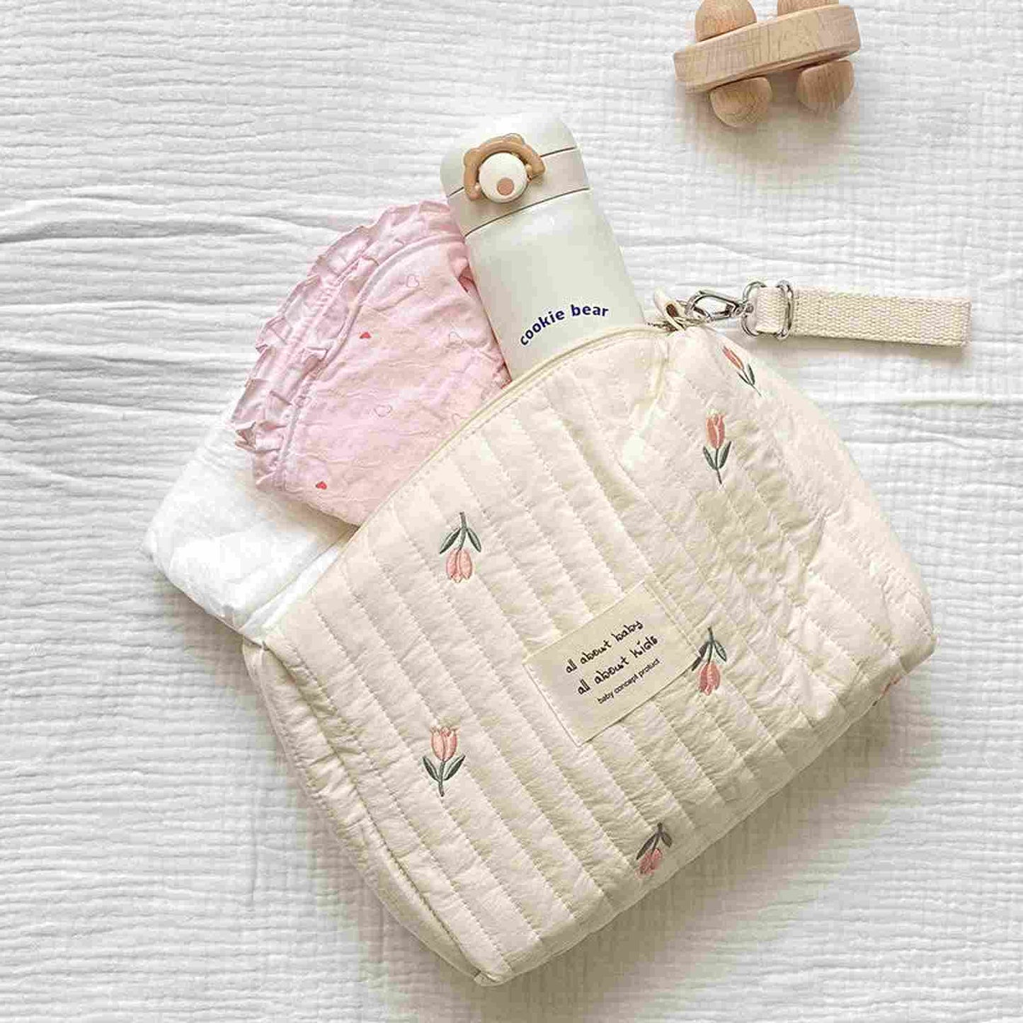 embroidered diaper bag with a diaper, burb cloth, and water bottle inside. Diaper bag is white with pink and green flowers