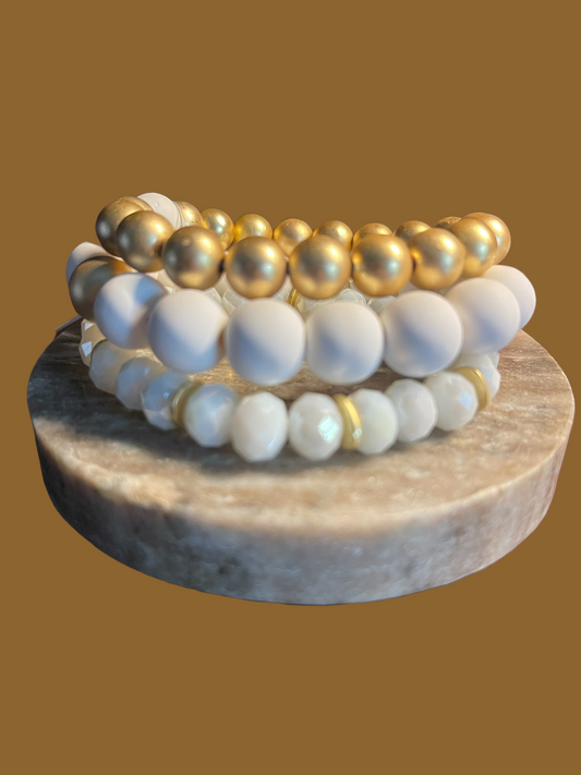 Stack of three bracelets, one gold, one white, one white beads with gold spacers