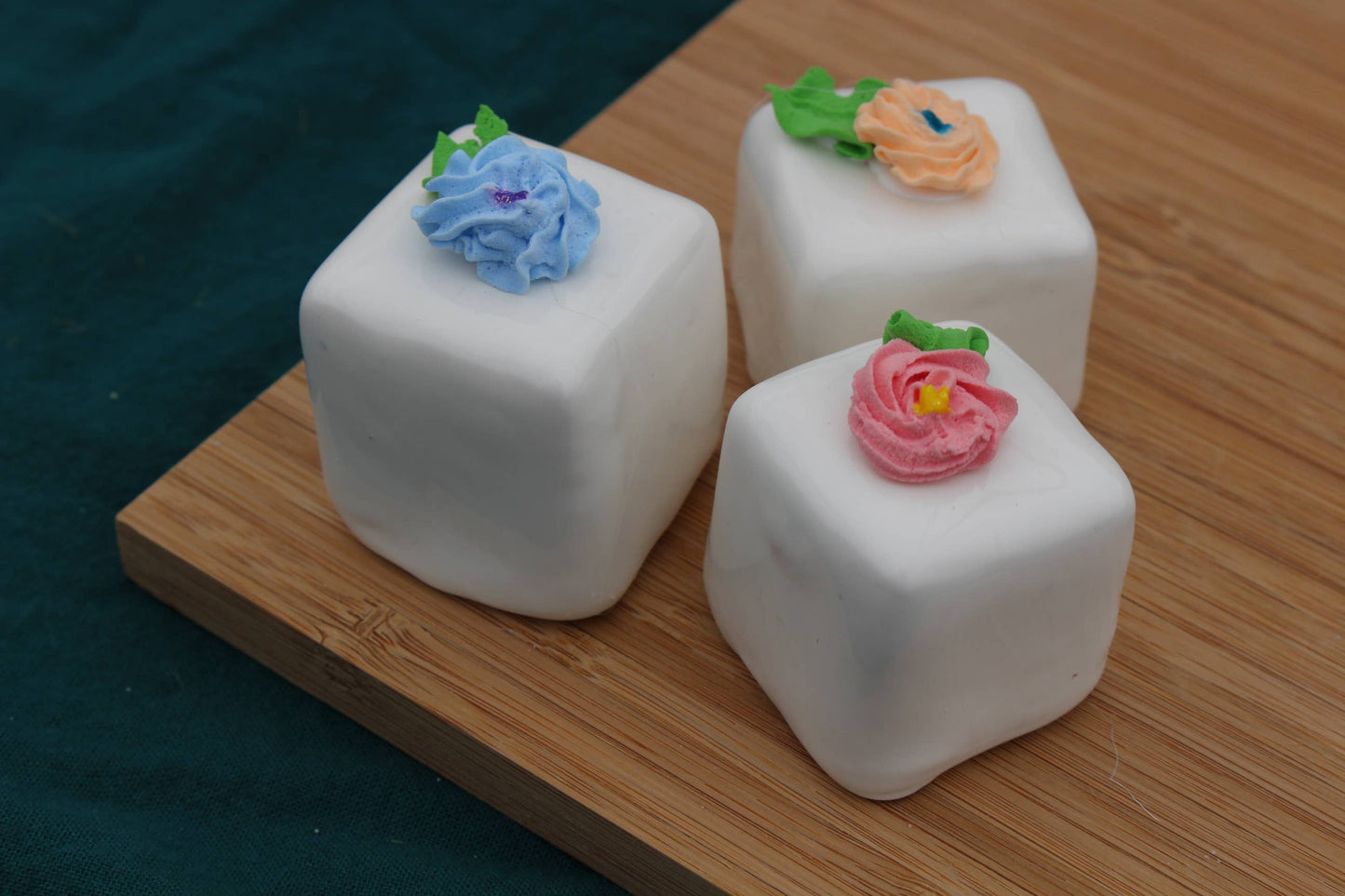Three large fake vanilla petit fours with blue, orange, and pink icing flowers on white icing. Available in large size only.