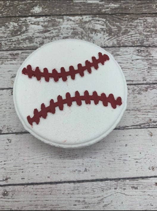 This is a baseball-shaped cookie, expertly handcrafted and decorated with red icing to depict stitches. Each one has been individually baked for a unique charm. Please note that due to the handmade nature of this product, there may be slight variations in shape and color.