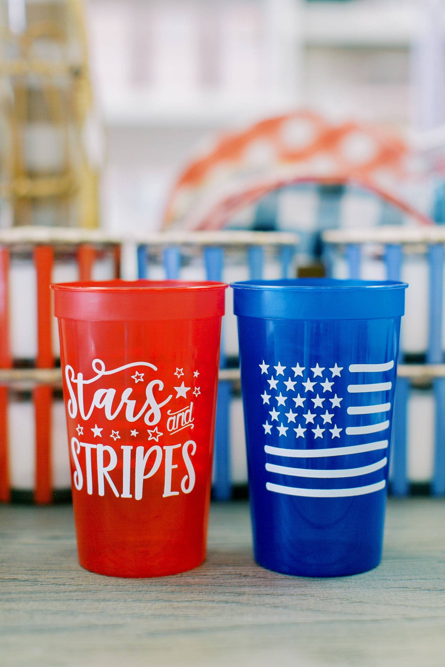 Two 22oz patriotic stadium cups: one red with "Stars and Stripes" in white text and stars, and one blue with a white stylized American flag. Available size: 22oz.