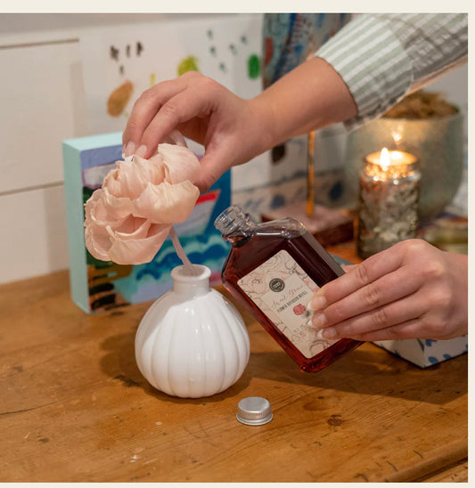 Sweet Grace Flower Diffuser Refill poured into a white vase with pink faux flower; available in 8oz and 16oz sizes.