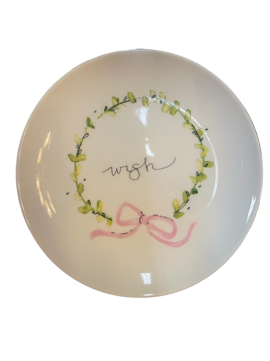 5” round stoneware plate with "wish" in center, green wreath, and pink ribbon bow. Available in 5” size only.