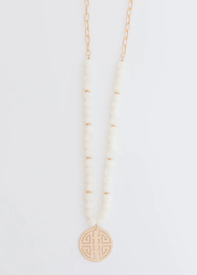 Gold chain with white beads and round geometric cut-out pendant. Available sizes: 16", 18", 20".