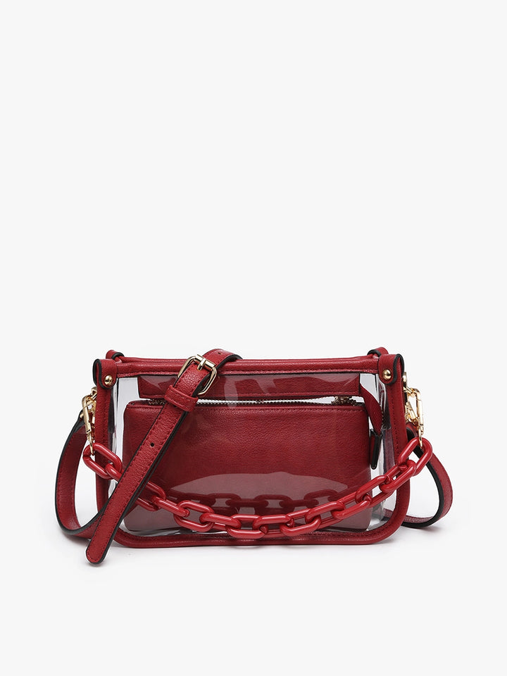 The Jessica Clear Crossbody is a red stadium-approved bag with transparent exterior, gold hardware, red chain detail, inner zippered pouch, and matching red shoulder strap. Size: 8" W x 6" H x 2.5" D.