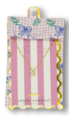 Gold cursive letter pendant necklace on pink and white striped packaging. Sizes available: small.