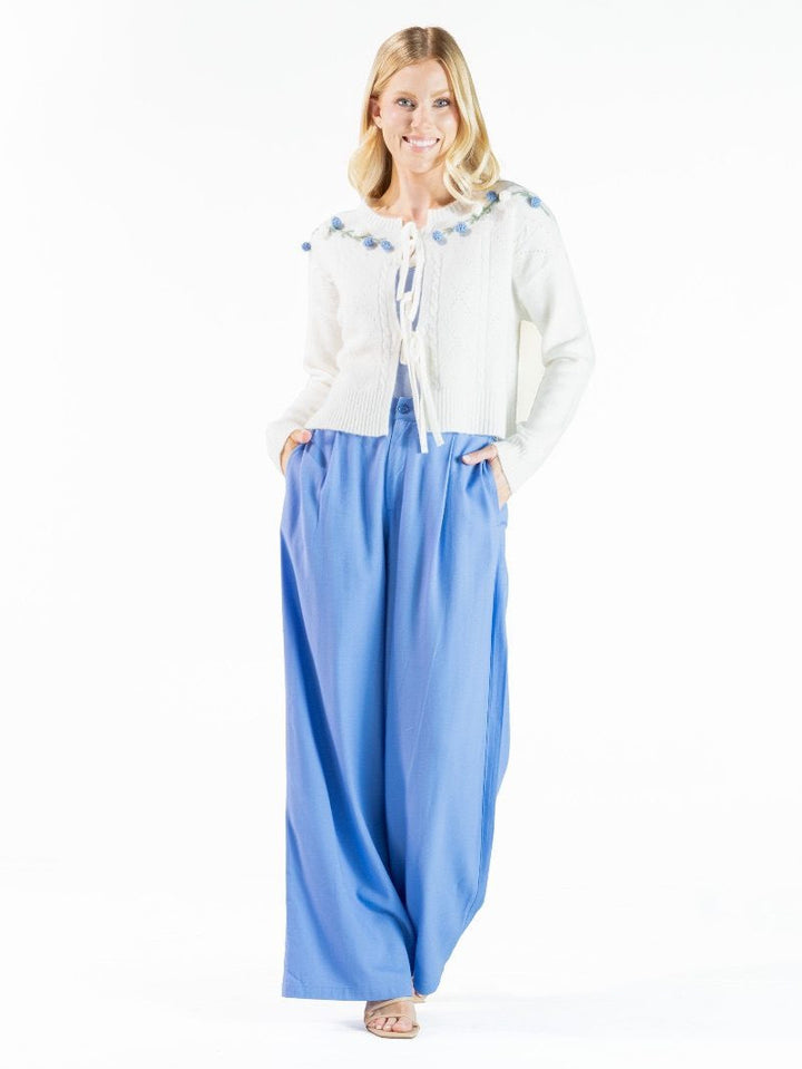 White textured cardigan with pom-pom details and neck tie. Available in sizes XS–XL.