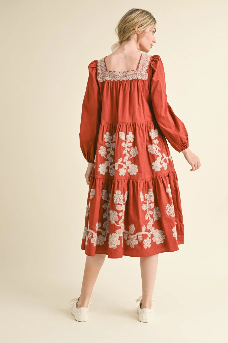 Rust, floral embroidered midi dress with long sleeves, square neckline, and tiered skirt. Available in various sizes.