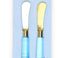 Set of two cheese spreaders with brushed gold blades and glossy light blue handles. Available in standard size.