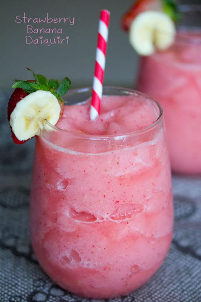 Pink strawberry banana daiquiri in glass with striped straw and fruit garnish. Available in 8oz, 16oz, and 32oz sizes.