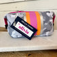 The Olivia Small Neoprene Makeup Bag has gray camo, pink, orange, and silver stripes. Comes in a small size with zipper closure.