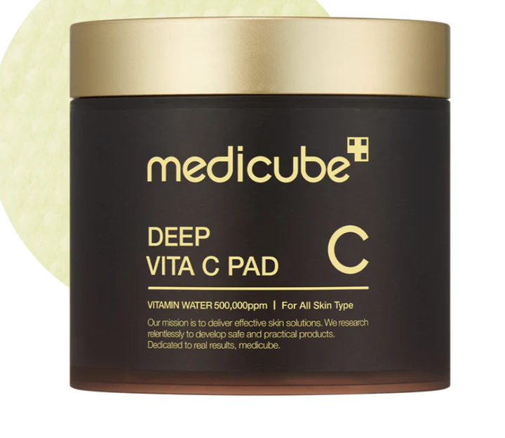 Dark brown MEDICUBE Deep Vita C Pads Brightening jar with gold lid, 70 pads per jar. Round yellow pad visible.