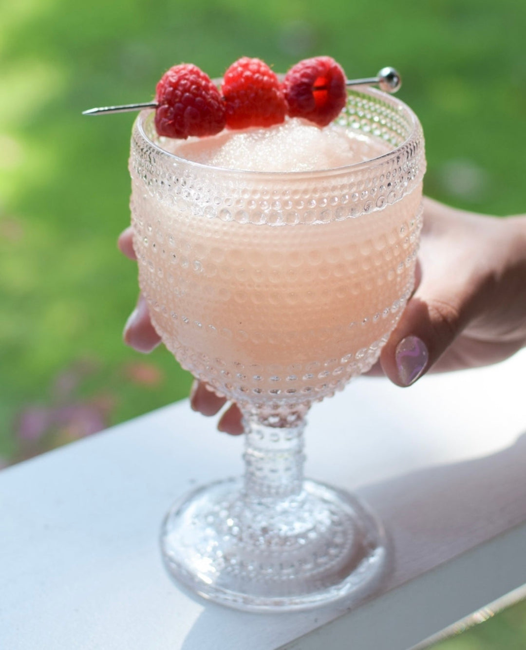 Textured glass of light pink Frosé Ready to Freeze Slush Mix, garnished with raspberries. Available in 4oz, 8oz, and 16oz sizes.