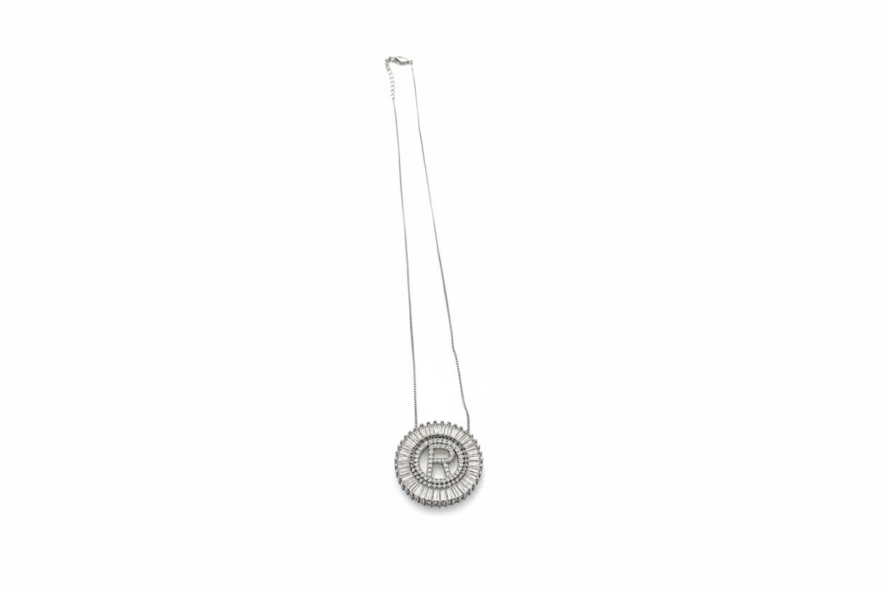 Silver circular pendant with bold "R," framed by sparkling stones. Available in 16", 18", and 20" chain lengths.