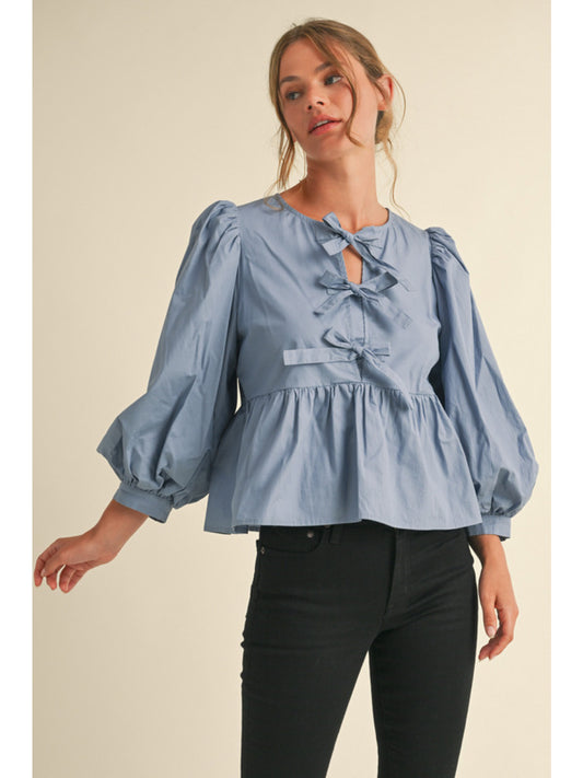 Bow Tie Peplum Top in light blue. Features puffy balloon sleeves and three decorative front bows. Sizes: XS, S, M, L.